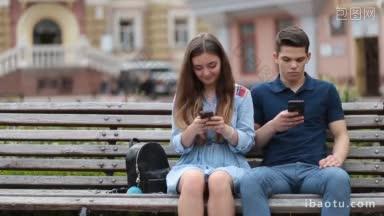 时髦的情侣坐在公园的长凳上，用智能手机浏览，表现出彼此的不感兴趣